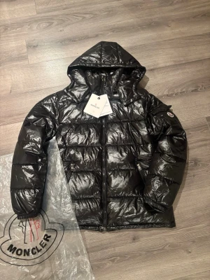 Moncler jacka svart - Snygg svart dunjacka från Moncler med glansig finish och huva. Loggan går att scanna. Storlek M men passar även S. Tags och påse tillkommer vid köp. Hör av dig vid frågor eller prisförs 