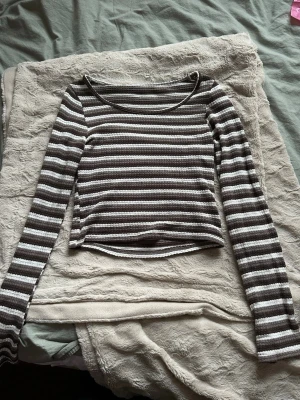 Brun och vit randig långärmad topp - Säljer en brun och vit randig långärmad topp med croppad passform. Toppen har rund halsringning och är gjord i ett ribbat och stickat material som ger en skön och stretchig känsla. Perfekt att styla med höga byxor eller kjol. Står storlek xl, men själv har jag xs och sitter ändå bra. Den är stretchig och kanske mer sitter som en m!