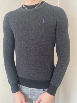 Mörkgrå stickad tröja Polo Ralph Lauren - Snygg o stilig mörkgrå tröja från Ralph Lauren med cool och unik lila logga på bröstet. Formar sig fint på kroppen. Passar till allt o funkar året om! Postar inom 24h📦 Köp mer än ett plagg för 10% rabatt!🤝 Tveka inte på att höra av er vid frågor eller funderingar!