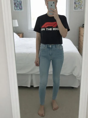 Svart F1 t-shirt med tryck - Cool svart t-shirt med F1-logga och texten 'ON THE EDGE' i vitt och rött framtill. Klassisk passform med rund hals och korta ärmar. Perfekt för dig som gillar motorsport och vill ha en statement-tee i garderoben.