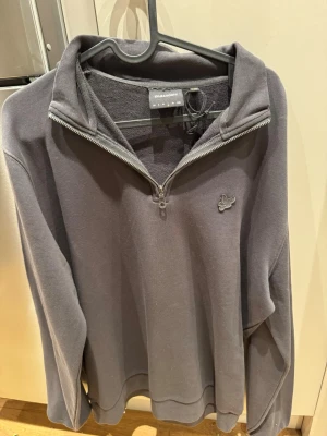 Grå halvzip från Lyle & Scott - Snygg grå tröja från Lyle & Scott med halv dragkedja och broderad logga på bröstet. Tröjan har en klassisk passform, ribbade muddar och är tillverkad i mjukt material som känns skönt mot huden. Perfekt för en avslappnad och stilren look.