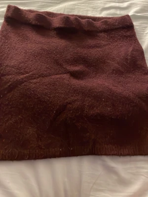 Vinröd ullkjol - Mysig vinröd kjol i ull med enkel, rak passform. Kjolen är kort och har en mjuk, lite luddig yta som ger en skön känsla. Perfekt att styla med stickade tröjor eller boots för en trendig look.