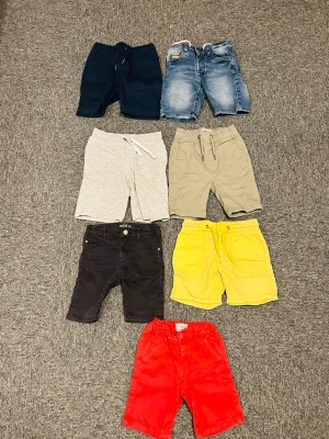 Färgglada shorts i olika material - Säljer ett paket med sju par shorts i olika färger och material. Färgerna är marinblå, ljusblå denim, ljusgrå, beige, svart, gul och röd. Några har snörning i midjan och vissa är i bomull eller denim. 