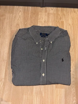 Ralph Lauren skjorta - Storlek xxl men passar XL Klassisk svartvit rutig skjorta från Polo Ralph Lauren med lång ärm och knappar framtill. Skjortan har button-down krage och broderad logga på bröstet. Perfekt för en stilren look.