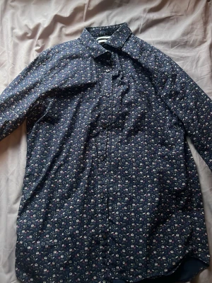 Blommig skjorta från Jack & Jones - Mörkblå skjorta från Jack & Jones med blommigt mönster i vitt, rosa och grönt. Slim fit-modell med långa ärmar och klassisk krage. Perfekt för dig som vill ha en skjorta med lite extra stil och detaljer.