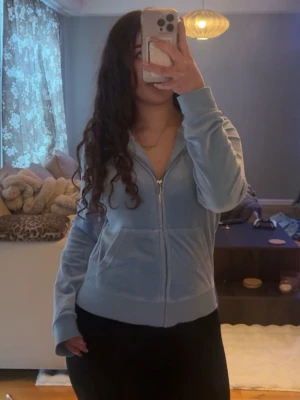 Ljusblå Juciy Cuoture - Säljer en ljusblå hoodie i mjuk velour med dragkedja framtill och fickor på sidorna. Hoodien har en klassisk huva och breda muddar vid ärmslut och nederkant. 