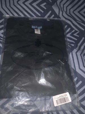 Svart t-shirt från Prada - Snygg svart t-shirt från Prada med klassisk logga framtill. T-shirten har rund hals och korta ärmar, perfekt för dig som gillar stilrena designer och exklusiva märken. Kommer i originalförpackning.