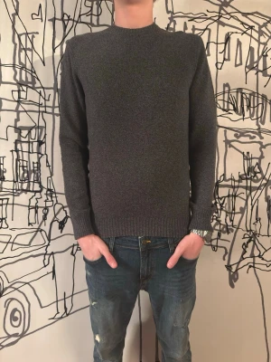 Stickad tröja - En enkel och stilren mörkgrå stickad tröja. Tröjan har rund halsringning, långa ärmar och ribbade muddar vid ärmslut och nederkant. Perfekt basplagg i garderoben och passar till det mesta.