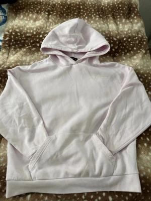 Ljusrosa hoodie från FB Sister - Säljer en ljusrosa hoodie från FB Sister i storlek S. Hoodien har en klassisk huva, magficka och ribbade muddar vid ärmslut och nederkant. Tillverkad i mjukt bomullsmaterial som känns skönt mot huden. Enkel och stilren design med liten vit text på bröstet.