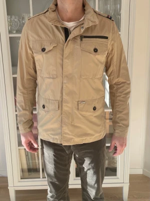 Beige Snoot Fieldjacka - M - Jag säljer den här snygga fieldjackan från Snoot som är perfekt nu till våren och sommaren. Den är i riktigt fint skick utan skador. Nypris låg på närmare 5000kr och jag säljer den för 599kr. Tveka inte att höra av er!