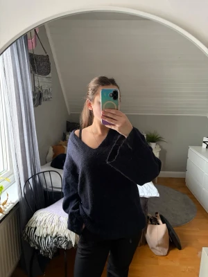 Marinblå oversize stickad tröja - Mysig marinblå stickad tröja med djup v-ringning och oversize passform. Långa ärmar och ribbstickade muddar. Perfekt för lager-på-lager och chill stil. Materialet ser ut att vara mjukt och fluffigt, troligen akryl eller ullblandning.