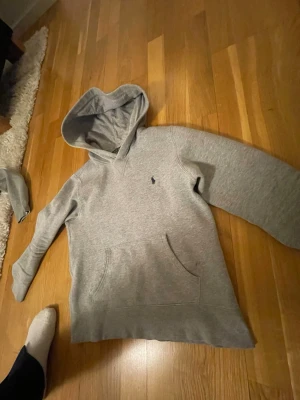 Grå hoodie från Polo Ralph Lauren - Snygg grå hoodie från Polo Ralph Lauren med klassisk huva och känguruficka. Diskret broderad logga på bröstet. Perfekt för en chill och avslappnad stil. Mjuk och skön bomullsblandning som passar året runt.