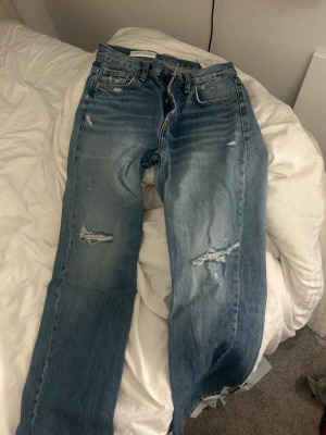 Blå slitna jeans med hål - Säljer ett par ljusblå jeans med slitningar och hål på båda benen, från Zara. Det är absolut inget fel på de, de kommer bara inte till användning💕
