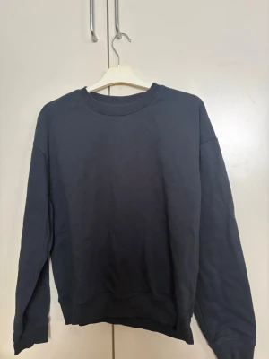 Mörkblå hoodie från 157, XS - En enkel och stilren mörkblå hoodie från 157 i storlek XS. Hoodien har rund halsringning, ribbade muddar vid ärmslut och nederkant samt en mjuk insida. Perfekt för en chill och avslappnad look.