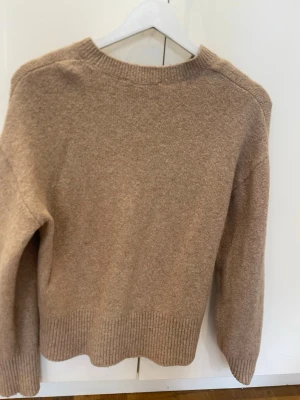 Beige stickad tröja i ullmix - Mysig beige stickad tröja med rund hals och ribbade muddar vid ärmslut och nederkant. Tröjan har en enkel, rak passform  som passar perfekt för kyligare dagar.