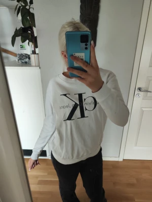 Calvin Klein långärmad topp - Två stilrena långärmade sweatshirts från Calvin Klein Jeans, en i vitt och en i grått. Båda har stor CK-logga framtill och rund hals. Tillverkade i mjuk bomull för skön känsla och avslappnad passform. De ser båda likadana ut bortsett från färgen därför fotade jag bara den vita