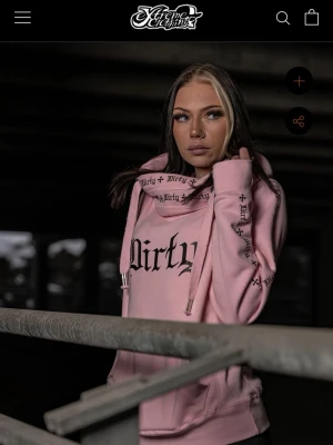Rosa hoodie från XtremeClothing - Säljer en ljusrosa hoodie från XtremeClothing med trycket 'Dirty' i svart på bröstet och textdetaljer längs huva och ärmar. Hoodien har stora snören, känguruficka och ribbade muddar. Perfekt för dig som gillar streetwear och vill sticka ut. Ordinarie pris 1000 kronor 