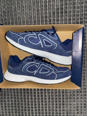 Blå sneakers med vita detaljer - Snygga blå sneakers från loggor på sidorna. Skorna har en kombination av mocka och mesh, vita tjocka sulor och svarta detaljer undertill. Perfekta för dig som vill ha en trendig och sportig look med exklusiv känsla.