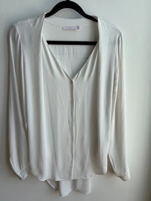 Viy blus från Wera - Stilren vit blus från Wera med v-ringning och knäppning framtill. Blusen har långa ärmar med knapp vid ärmslut och är tillverkad i ett mjukt, lätt material som faller snyggt. Perfekt till jeans eller kjol för en clean look. Köpare står för frakt. 