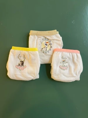 Disney trosor med Frost-motiv - Tre par ljusa trosor med motiv från Disney Frost, bland annat Olaf och Sven. Varje par har olika färg på resåren: gul, beige och rosa. Mjukt material, bomull, och bekväm passform. Perfekta för dig som gillar söta och lekfulla underkläder.