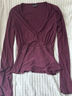 Vinröd omlottopp med spets från Gina Tricot - En vinröd omlottopp från Gina Tricot med lång ärm och spetsdetalj under bysten. Toppen har en v-ringad skärning och sitter figurnära. Är i storlek xxs! Endast provat och inte använd. 