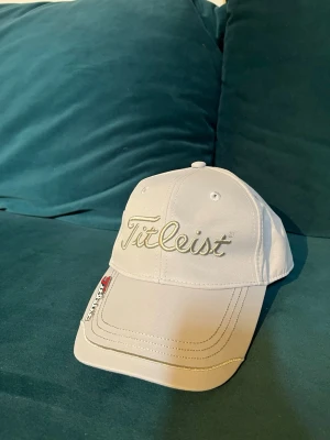 Grå Titleist keps med broderad logga - Snygg vit keps från Titleist med broderad logga framtill och justerbart spänne bak. Klassisk böjd skärm och stilren design, perfekt för golf eller vardagsstil. Tillverkad i slitstarkt tyg som andas.