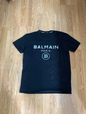 Svart Balmain Paris t-shirt - Snygg svart t-shirt från Balmain Paris med stort vitt tryck på bröstet och rund hals. Klassisk passform och tillverkad i mjuk bomull som känns skön mot huden. Perfekt för dig som gillar exklusiva streetwear-vibbar.