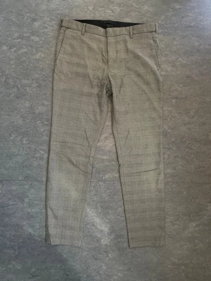 Rutiga skinny fit kostymbyxor H&M - Säljer ett par rutiga kostymbyxor från H&M i skinny fit-modell. Byxorna har ett klassiskt svartvitt rutmönster, bälteshällor och smal passform. Perfekta för dig som gillar en stilren och modern look.