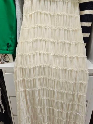 Vit långklänning med volangdetaljer - Supersnygg vit långklänning med volangdetaljer i hela tyget. Klänningen har en ärmlös design med hög hals och smickrande passform. Perfekt för sommarens alla tillfällen och ger en romantisk vibe. Materialet känns lätt och luftigt.  Polyester (oftast 95 % till 100 %). Storlek S&M