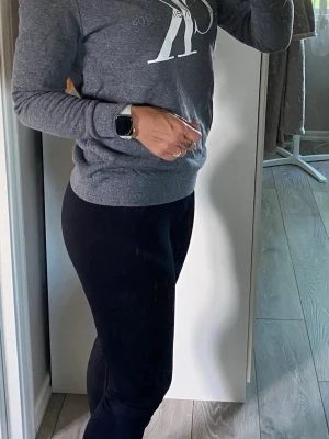 Grå Calvin Klein sweatshirt - Mysig grå sweatshirt från Calvin Klein Jeans med stort vitt CK-tryck på bröstet. Tröjan har rund halsringning, ribbade muddar vid ärmslut och nederkant samt en avslappnad passform. Perfekt för en casual och trendig look.