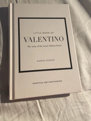 Little Book of Valentino av Karen Homer - Stilren och inspirerande bok med vit hård pärm, svart text och grafisk design. 'Little Book of Valentino' berättar historien om det ikoniska modehuset Valentino, skriven av Karen Homer. Perfekt för dig som älskar mode och design.