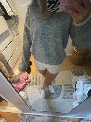 grå stickad tröja - En grå stickad tröja med avslappnad passform och rund hals. Tröjan har långa ärmar och ribbade muddar vid ärmslut och nederkant. Perfekt för lager på lager och en chill vibe. Materialet ser ut att vara mjukt och mysigt, troligen en ull- eller akrylblandning.