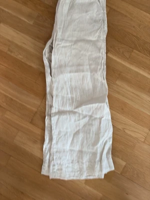 Beiga vida linnebyxor med resårmidja - Säljer ett par beiga linnebyxor med avslappnad passform och resår i midjan. Byxorna har raka ben och sidofickor, perfekta för en chill och luftig stil. Materialet är linne som ger en skön känsla och snygg struktur. Fint skick, men tagit bort snöret i midjan! Märke: OYSHO
