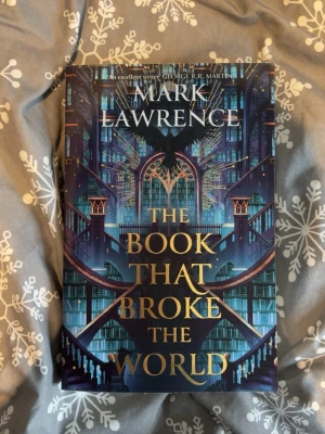 The Book That Broke the World - En fantasifull roman av Mark Lawrence med en färgstark och detaljerad omslagsdesign i blått, lila och guld. Boken är på engelska och tillhör Library Trilogy. Perfekt för dig som gillar episka äventyr och magiska bibliotek.