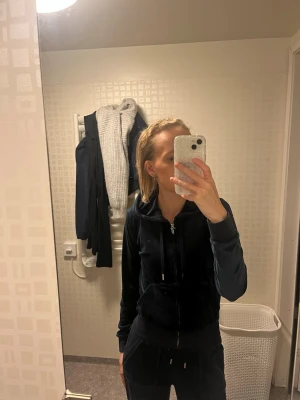 Mörkblå set Juicy Couture - Säljer en mörkblå velour set  från Juicy Couture med dragkedja och huva. Hoodien har matchande snören med guldfärgade metalldetaljer och ett broderat JC-logotyp på bröstet. Perfekt för en chill och trendig look. Liten bit längst ner på juicy märket som har lossnat men de är inget man tänker på väldigt fint skick för övrigt byxorna är i XXS men passar perfekt på mig som är XS vanligtvis nypris 2500