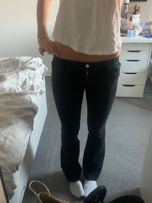 Svarta bootcut jeans med låg midja - Säljer ett par svarta bootcut jeans med låg midja och klassisk femficksmodell. Jeansen har en snygg passform som sitter tajt över låren och släpper ut vid vaden. Perfekta till en trendig vardagslook. Passar mig som är 167, den har ett litet hål ( se sista bilden)