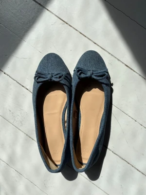 Blå denim ballerinaskor med rosett - Snygga ballerinaskor från H&M i blått denimtyg med en söt rosett framtill. Skorna har rund tå och beige innersula för extra komfort. Perfekta för dig som gillar en avslappnad men trendig stil.