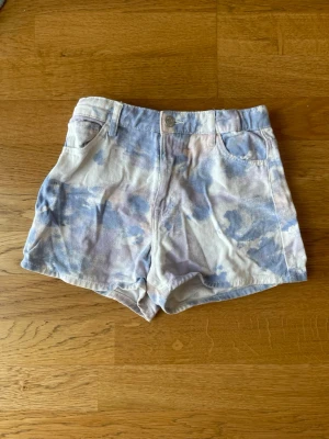 Blåvit tie-dye shorts i bomull - Snygga blåvita tie-dye shorts med hög midja och klassisk femficksdesign. Gjorda i mjuk bomull med knapp och dragkedja framtill. Perfekta för varma dagar och en avslappnad stil. 10-11 år