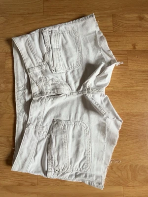 Vita denimshorts med rå kant - Snygga vita shorts i denim med råa kanter och flera fickor fram och bak. Klassisk femficksmodell med dragkedja och knapp. Perfekta för varma dagar och enkel att matcha med allt. Passar dig som gillar en avslappnad och trendig stil.