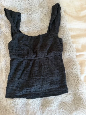 Svart linnetopp med struktur - Säljer en svart linnetopp med breda axelband och snygg strukturerad yta. Toppen har en enkel och stilren design som passar perfekt till jeans eller kjol. Materialet känns lätt och bekvämt mot huden. Supersöt inför sommaren och jätte mjuk material, storlek xs.🖤