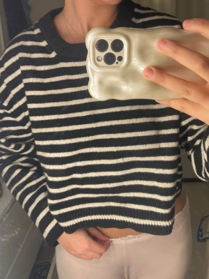 Svartvit randig stickad tröja - Stickad tröja med svarta och vita horisontella ränder. Modellen är croppad och boxig med rund halsringning och ribbade muddar vid ärmslut och nederkant. Materialet känns mjukt och bekvämt, perfekt för en chill och trendig look.