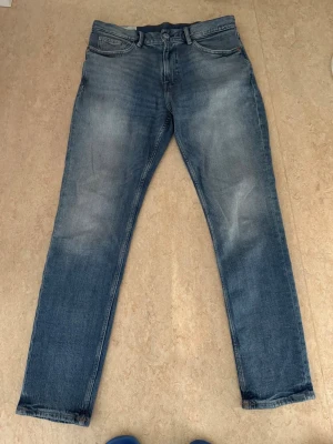 Blå raka jeans med slitningar - Snygga blå jeans med raka ben och diskreta slitningar på låren och knäna. Klassisk femficksmodell med dragkedjegylf och bälteshällor. Jeansen har en tvättad look och är tillverkade i denim.