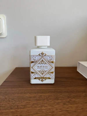 Bade'e Al Oud Honor & Glory parfym - Bade'e Al Oud Honor & Glory från Lattafa är en parfym i en vit, fyrkantig flaska med guldiga och geometriska detaljer. Doften har söta, varma kryddiga och fruktiga toner med inslag av vanilj, trä, puder, kanel och tropiska noter. Passar både kvinnor och män.