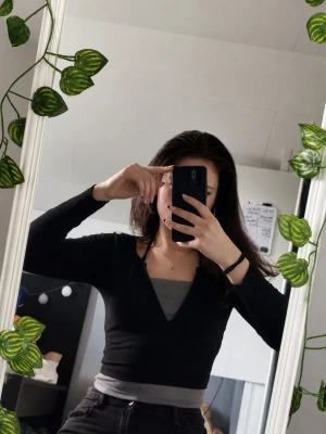 Svart topp med knappar - Trendig svart topp med v-ringning och knappar framtill. Långärmad och croppad modell som sitter tight. Toppen är ribbad och i mjukt material, perfekt att styla med jeans eller kjol.