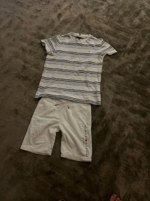 Randig t-shirt från Tommy Hilfiger - Snygg vit t-shirt lätt frotté från Tommy Hilfiger. Strl 164  Klassisk passform och korta ärmar. Liten logga broderad på bröstet. Perfekt till jeans eller shorts för en avslappnad stil. Vita shorts Tommy Hilfiger. Strl 152. 100 kr per plagg 