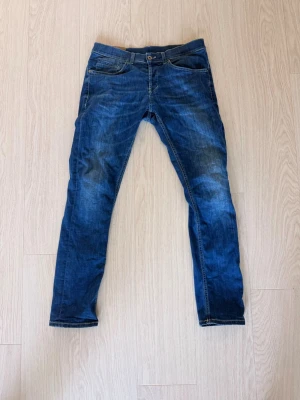 Blå Dondup Jeans  - Snygga blå dondup jeans med lätt slitna detaljer och klassisk femficksdesign. Jeansen har normal midja och smala ben, perfekta för en avslappnad och trendig look. Materialet är denim i bomull med lite stretch för extra komfort. Jeansen är knappt är varsamt använda.