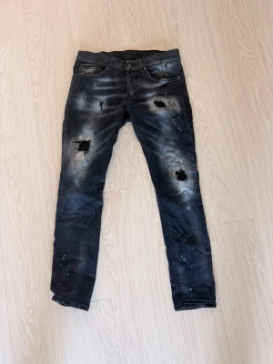 Svarta distressed Dondup jeans  - Säljer ett par svarta dondup jeans med slitningar på benen samt coola färgstänk. Jeansen har fem fickor och en tvättad look som ger en edgy streetkänsla. Perfekta för dig som gillar en tuff och trendig stil. Jeansen är inköpte på united fashion Göteborg för över 4 Tusen  och inte använda så mycket.