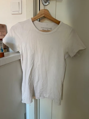 Vit basic t-shirt från Flash Essentials - En klassisk vit t-shirt från Flash Essentials med rund hals och korta ärmar. Tillverkad i mjuk bomull för en skön och enkel stil. Perfekt att matcha med allt i garderoben.
