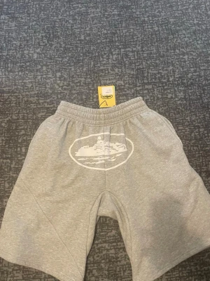 Grå sweatshorts med tryck - Gråa sweatshorts med elastisk midja och ett vitt tryck framtill. Shortsen har en bakficka med knapp och är tillverkade i mjukt bomullsmaterial. Perfekta för en avslappnad stil.