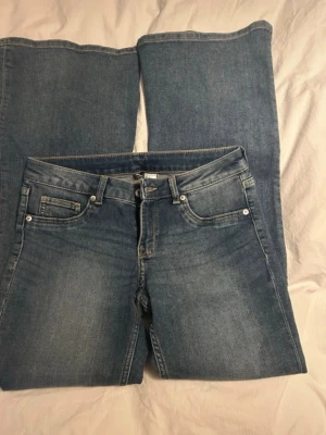 Blå bootcut jeans med klassisk tvätt - Snygga blå bootcut jeans med klassisk femficksmodell och ljus tvätt. Jeansen har normal midja, dragkedjegylf och silverfärgade nitar. Perfekta för dig som gillar en retroinspirerad look med utsvängda ben.
